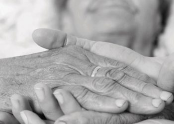 Caring nurse holding kind elderly lady's hands in bed.
** Note: Shallow depth of field